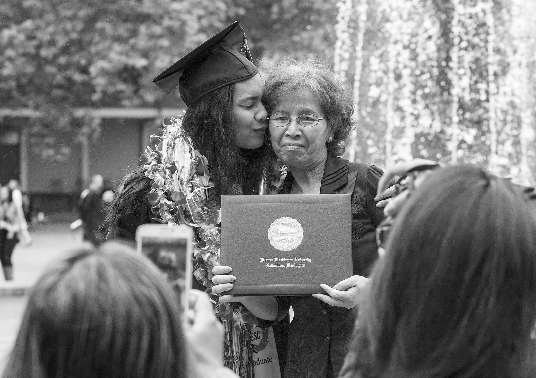 A western grad wearing a lei and kissing her mom on the cheek